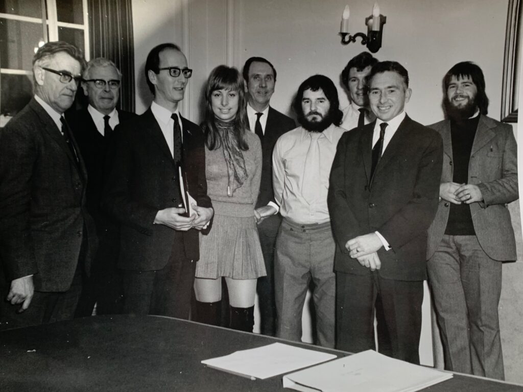 A black-and-white group photograph featuring nine people, standing in a formal pose.